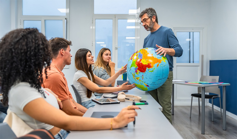 Educator with students in classroom and using a globe