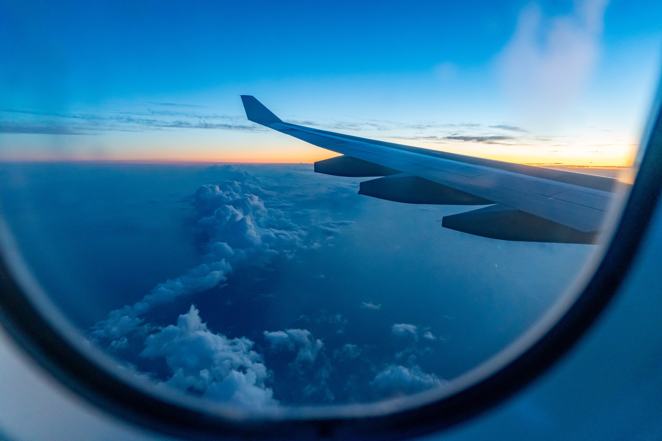 looking out an airplane window, seeing the wing flying above the clouds