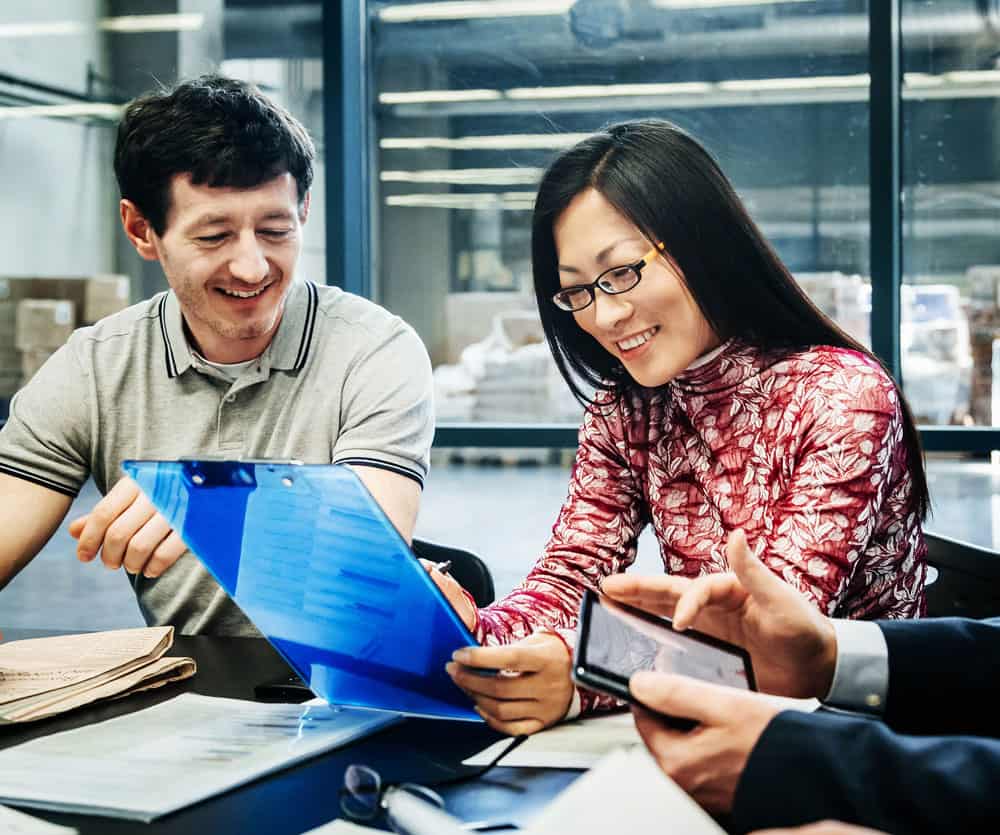 two colleagues in a conference room in manufacturing facility looking at clipboard