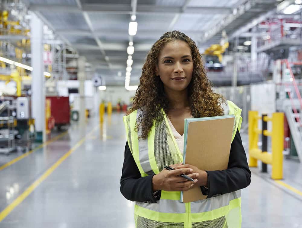 woman wearing safety vest in factory holding a notebook