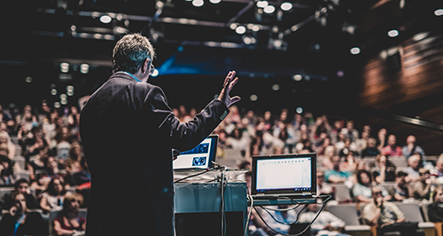 Medical device industry expert giving a speech in a full auditorium at an event.
