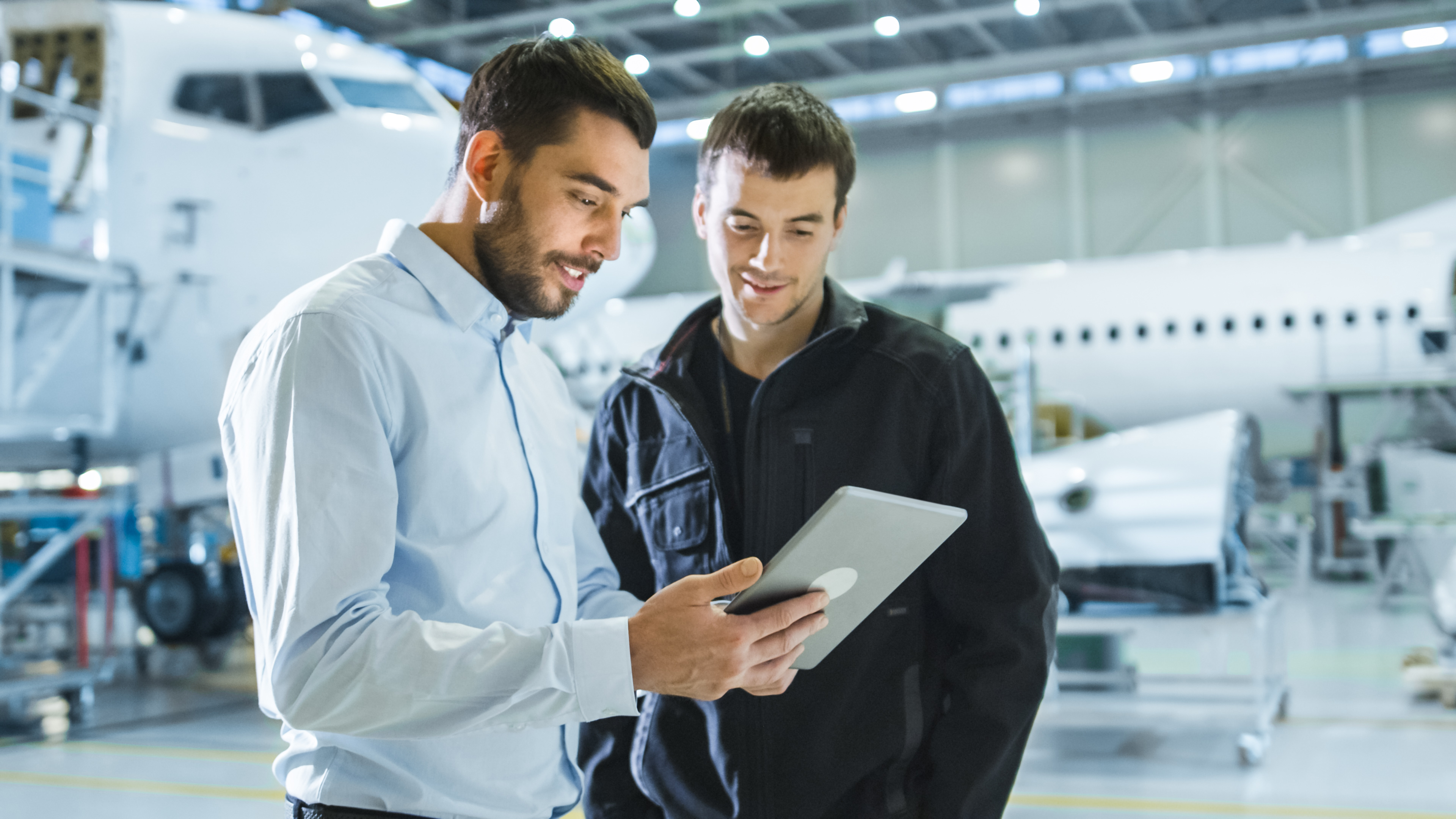 two men in airplane facility, one on tablet