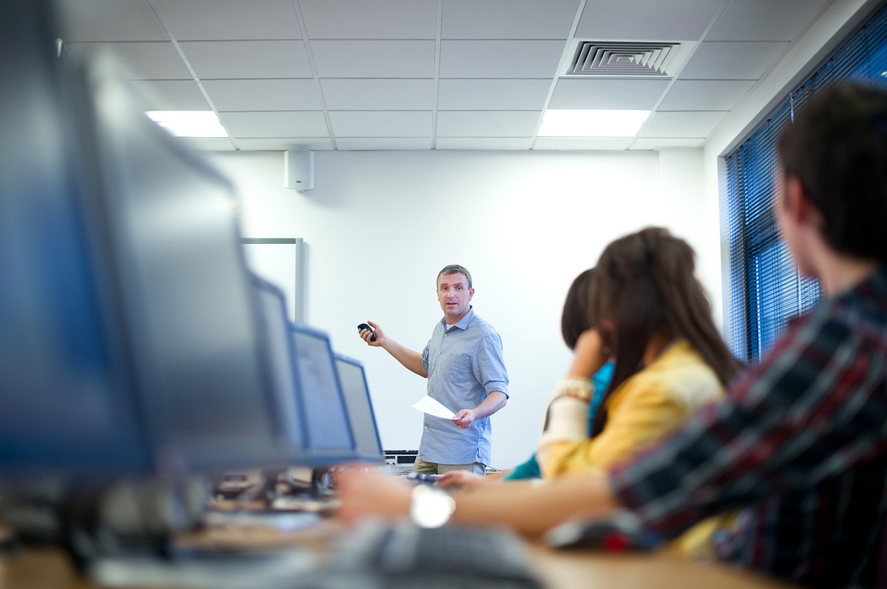 three aerospace professionals seated in a classroom setting while they attend a hosted PRI Training critical process course onsite while a subject matter expert stands and instructs the class.